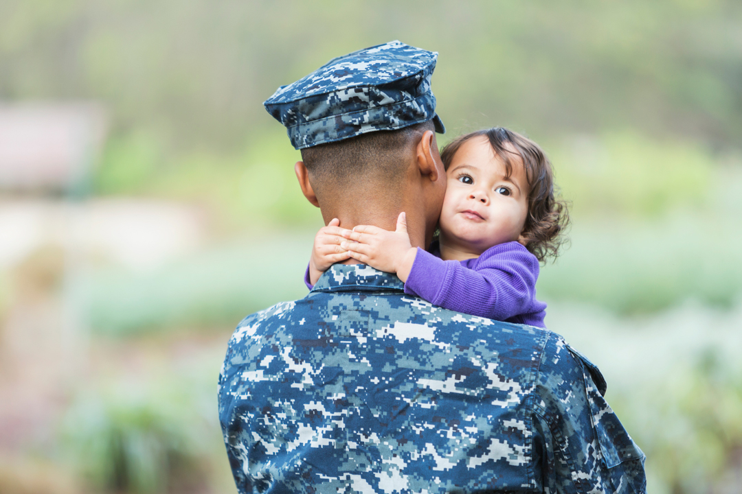 Man in uniform with little girl hugging his neck.