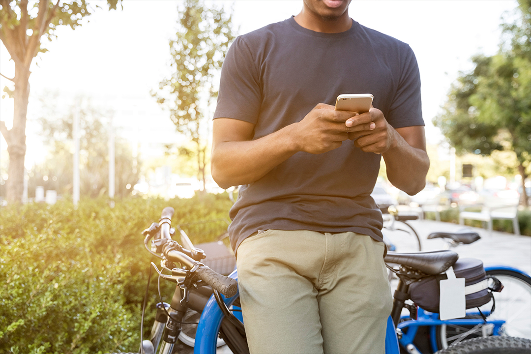 Guy leaning against his bicycle and looking at his mobile device on a sunny day.