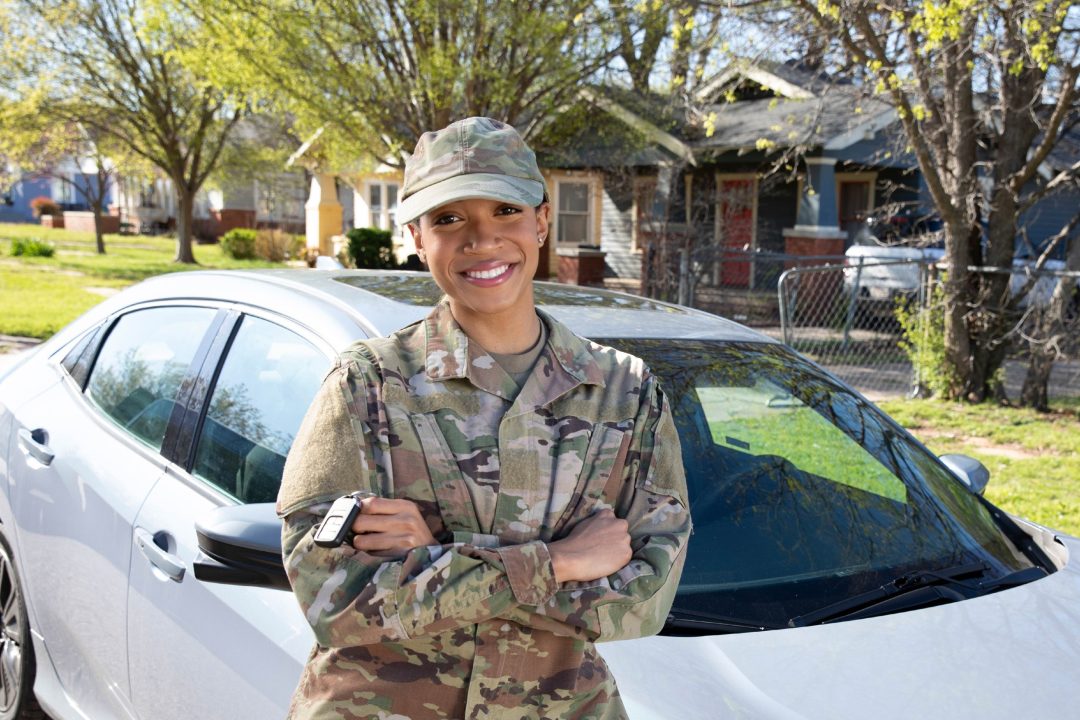 A woman in military uniform leaning against a white vehicle