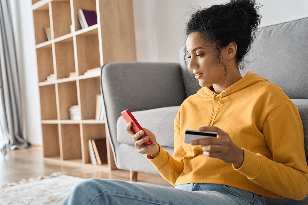 Young woman sitting on the floor on her smartphone and holding a card