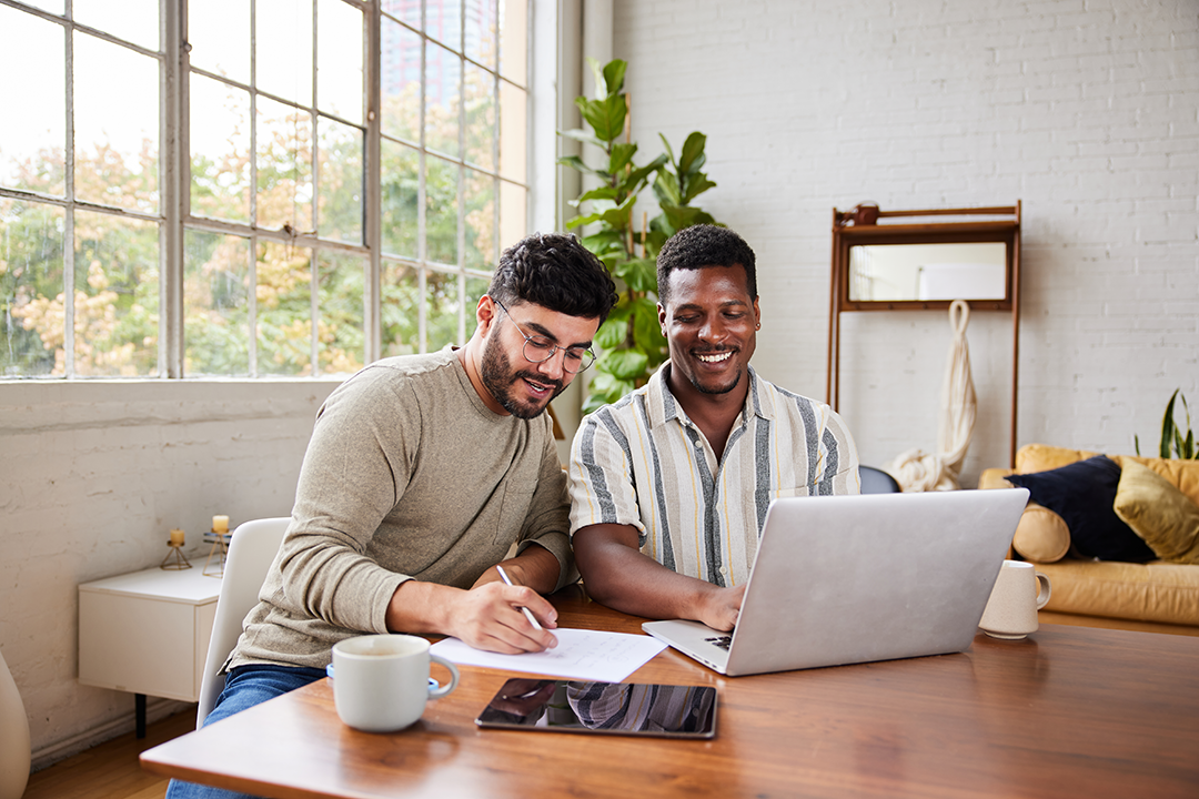 Two men working on a laptop and looking at a some paper.