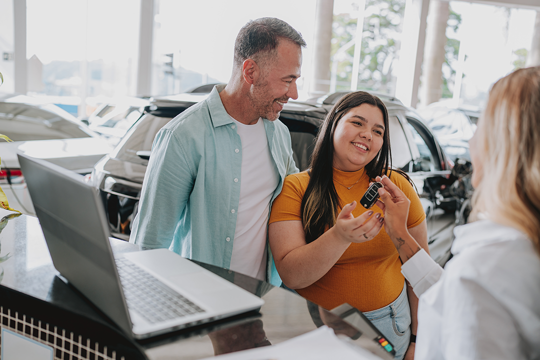 A dad standing with his daughter has she holds a car key.