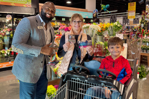 A mom holding up a gift card with her son and a TFCU employee.