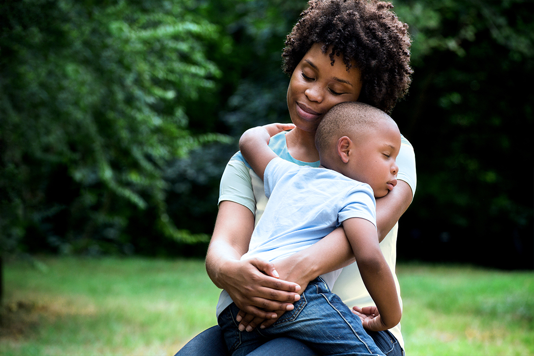 Mom sitting outside and lovingly holding son in lap.