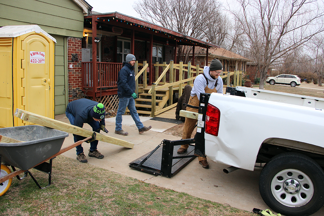 Three men are unloading a white truck in front of a house