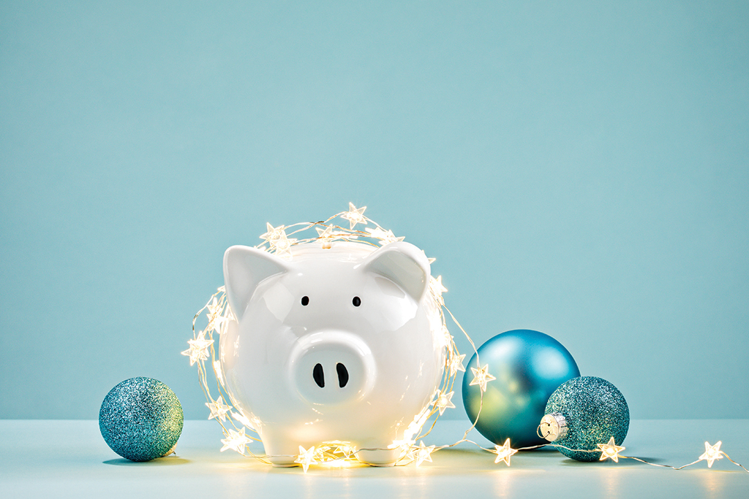 White piggy bank wrapped in holiday lights and surrounded by ornaments.