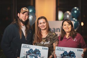 A man and two women who are TFCU members are holding two TFCU gift card signs.