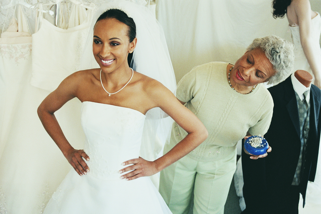 Young woman trying on white wedding dress, while older woman helps her with the dress fitting.