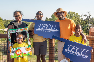 A mom, dad and three kids holding up oklahoma-shaped signs and a zoo photo sign.