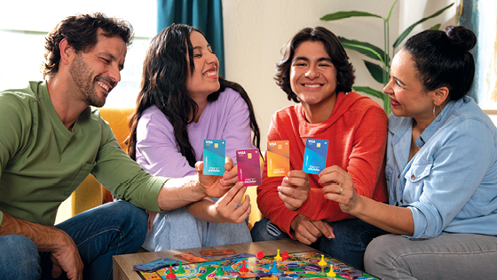 A family of four looking at the camera and smiling while holding up MoneyPlus cards