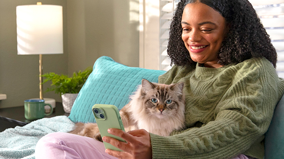Young woman sitting in bed on her mobile phone with her cat.