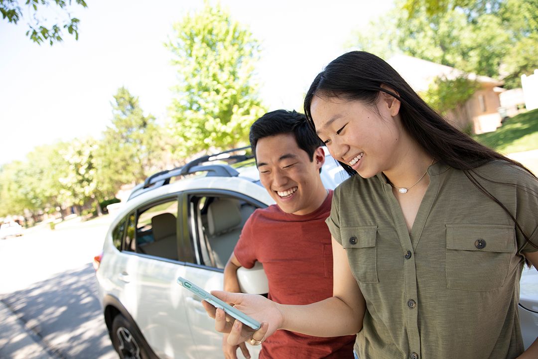 Two young adults standing in front of a car and looking at a mobile device