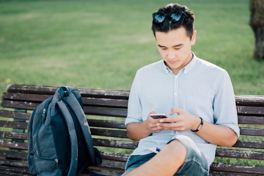 Man with backpack sitting on bench in park.