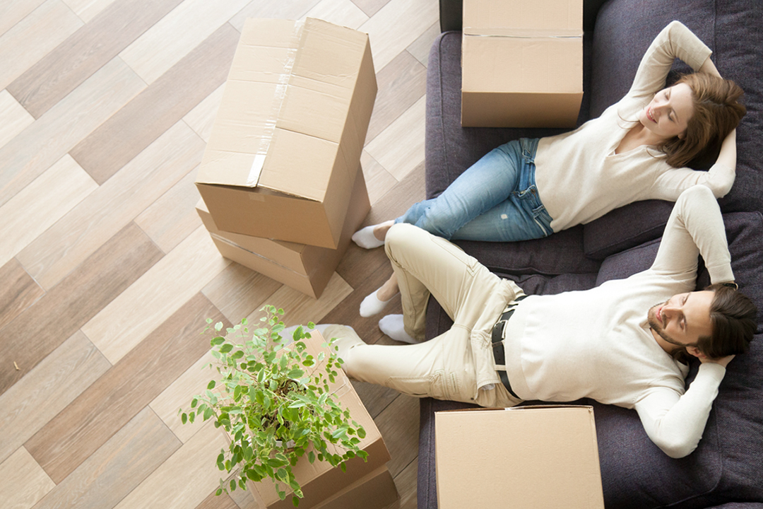 Man and woman relaxing on couch, surrounded by packing boxes.