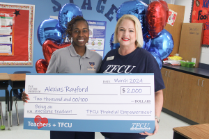 A TFCU employee standing with a teacher and holding up a large check sign.