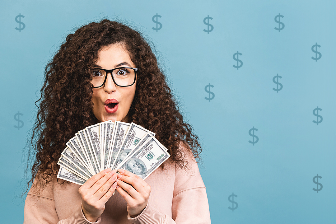 Woman holding up a fan of money with a blue background with dollar signs