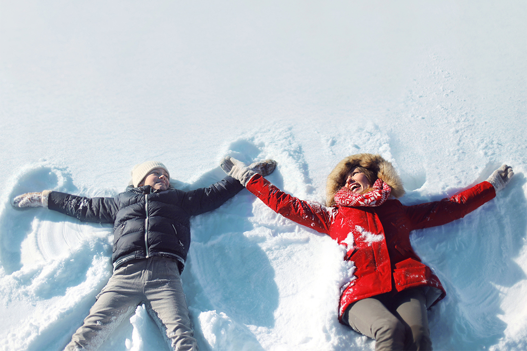 Child in black coat and woman in red coat making snow angels.