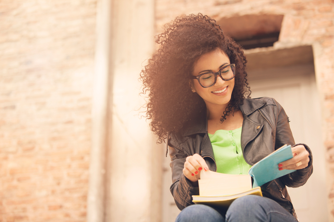 Young, happy woman in glasses looking at a book on her lap.