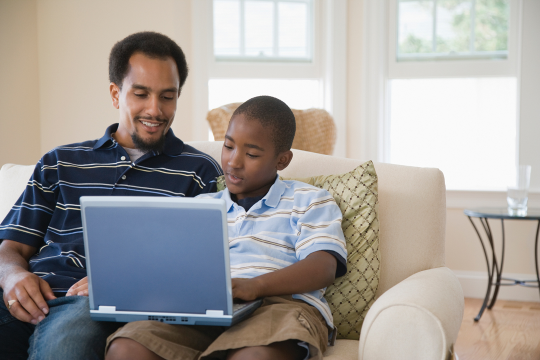 Father and son sitting on couch looking at laptop computer